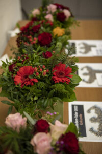 Vier verschiedene Blumensträuße stehen aufgereiht auf einem Tisch. Davor liegen Urkunden mit der Überschrift "Neuwieden - Taler 2022".