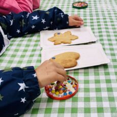 Nahaufnahme von Kinderhänden, die Kekse mit bunten Perlen verzieren.